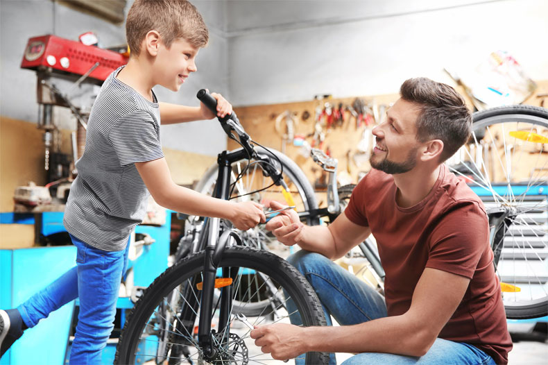 This image shows a man and a boy fixing a bike in a garage.
