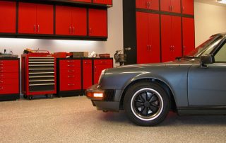 This image shows a garage floor, A classic gray car is parked there. Behind the car is a cabinet.